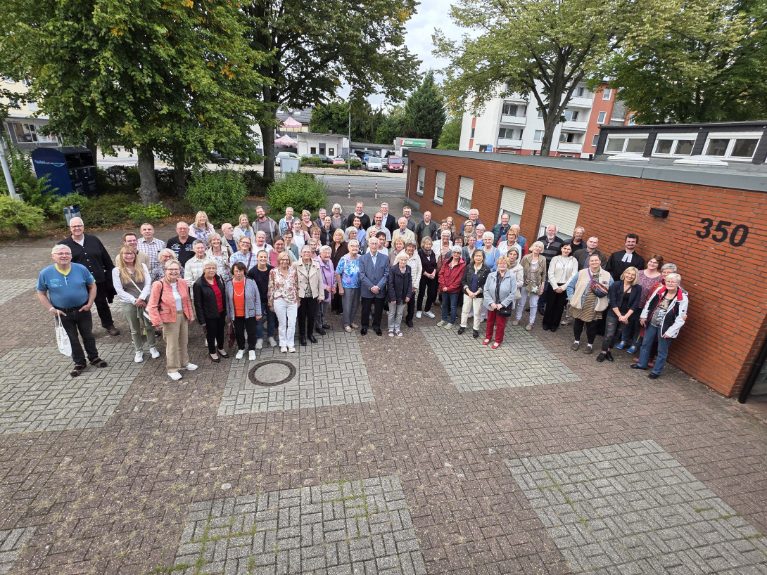 Gruppenfoto einer Vielzahl von haupt- und ehrenamtlichen Mitarbeitenden unterschiedlichen Alters, die auf dem Kirchvorplatz stehen.