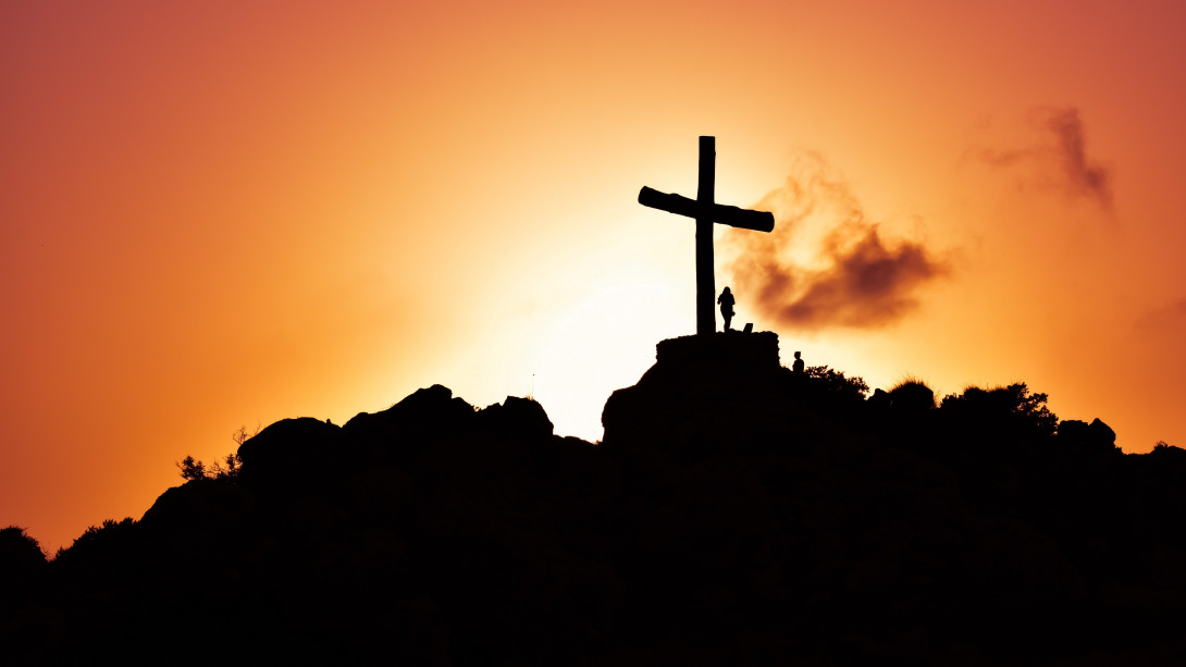 Ein großes Kreuz und eine schemenhaft erkennbare Person auf einem Hügel. Im Hintergrund der Sonnenaufgang.
