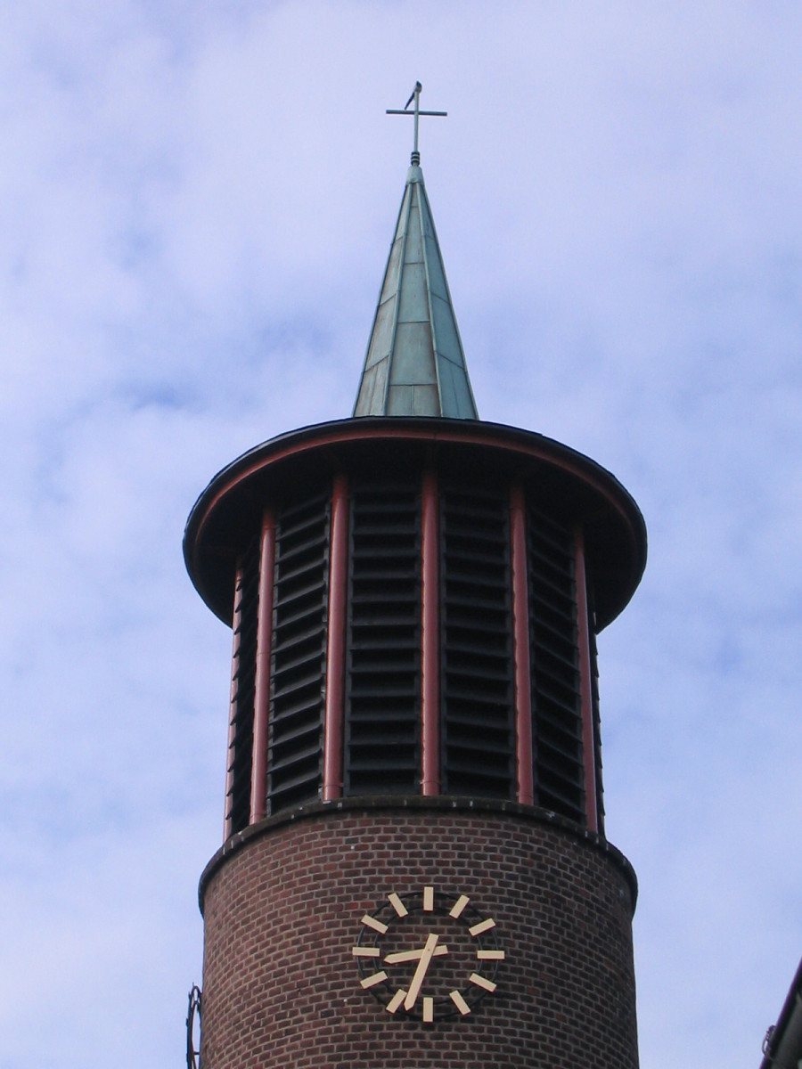 Glockenturm mit Kreuz als Spitze und Vogel oben drauf vor bewölktem Himmel